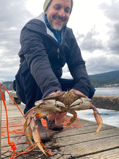 Person crouching on dock holding a crab with crab trap