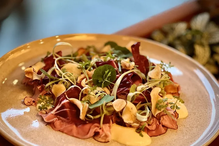 Gourmet salad with greens, radicchio, roast beef, and garnishes on a beige plate.