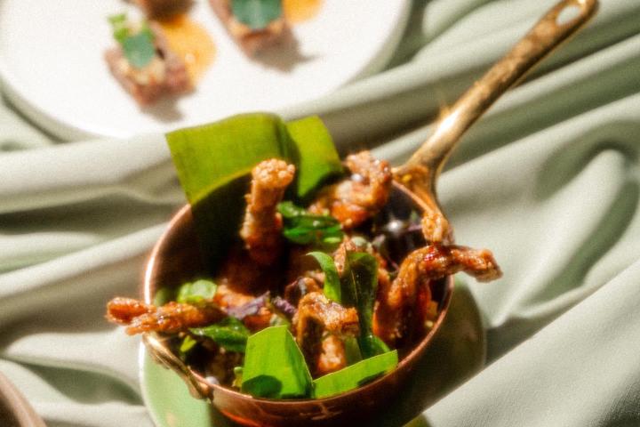 Close-up of a dish with crispy fried food in a copper pan and appetizers on a white plate.