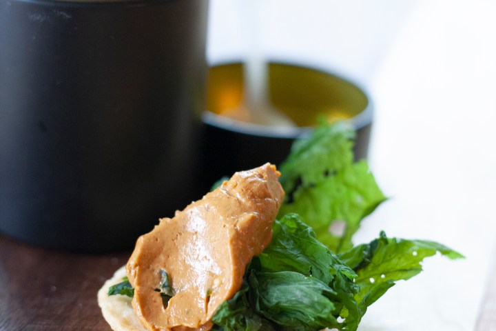 Cracker with peanut butter and greens near a black container on a table.